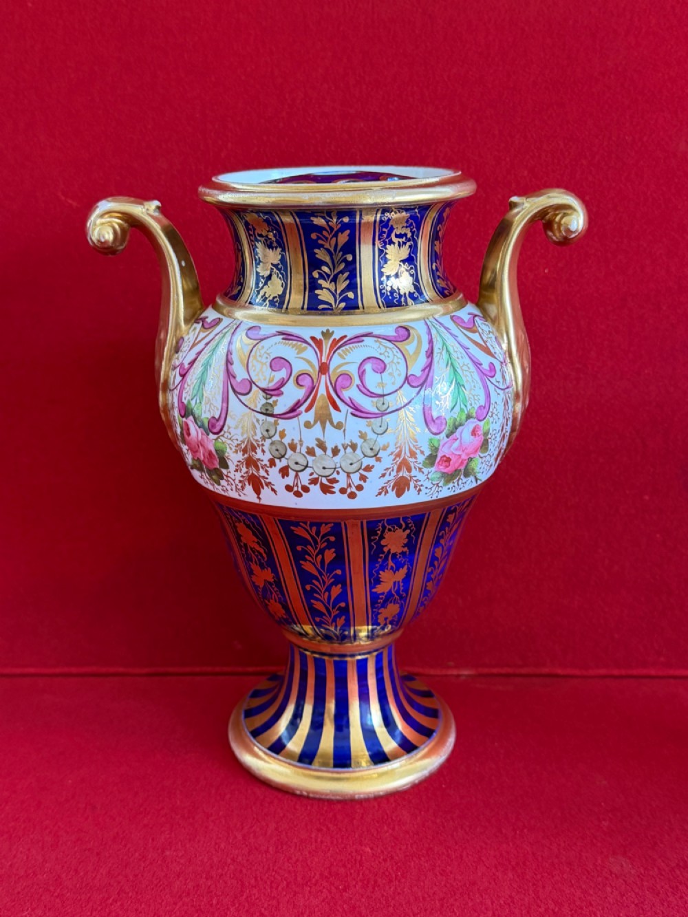 A three-piece English Regency Spode porcelain garniture featuring a central twin-handled urn flanked by two beaker-shaped vases decorated with cobalt blue panels, hand-painted pink floral motifs, and detailed gilt scrollwork. View VI