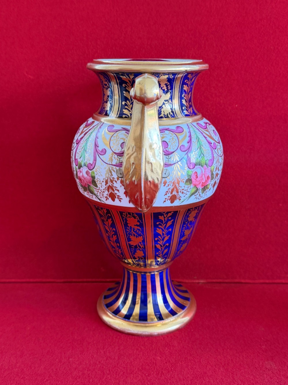 A three-piece English Regency Spode porcelain garniture featuring a central twin-handled urn flanked by two beaker-shaped vases decorated with cobalt blue panels, hand-painted pink floral motifs, and detailed gilt scrollwork. View VII