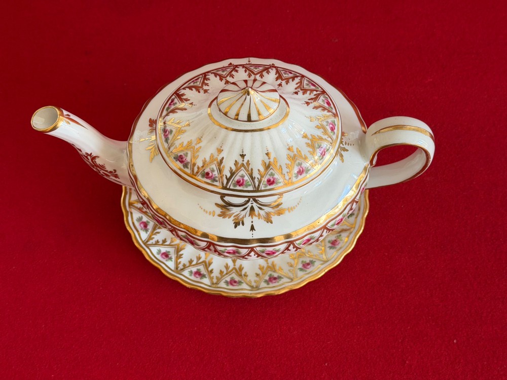 An 18th-century fluted white porcelain teapot and matching oval stand decorated with hand-painted pink floral motifs and gilded geometric borders. View V