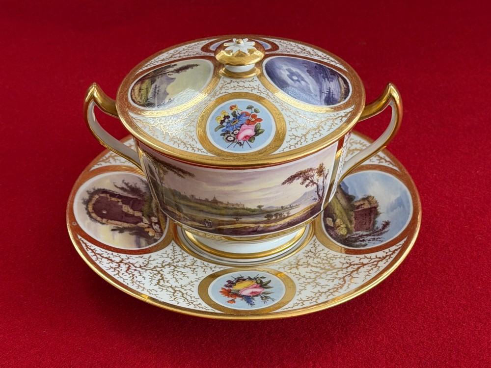 An antique Flight, Barr and Barr Worcester porcelain covered chocolate cup with two handles and matching saucer, decorated with hand-painted landscape and floral panels amid gold vermicelli detailing. View III