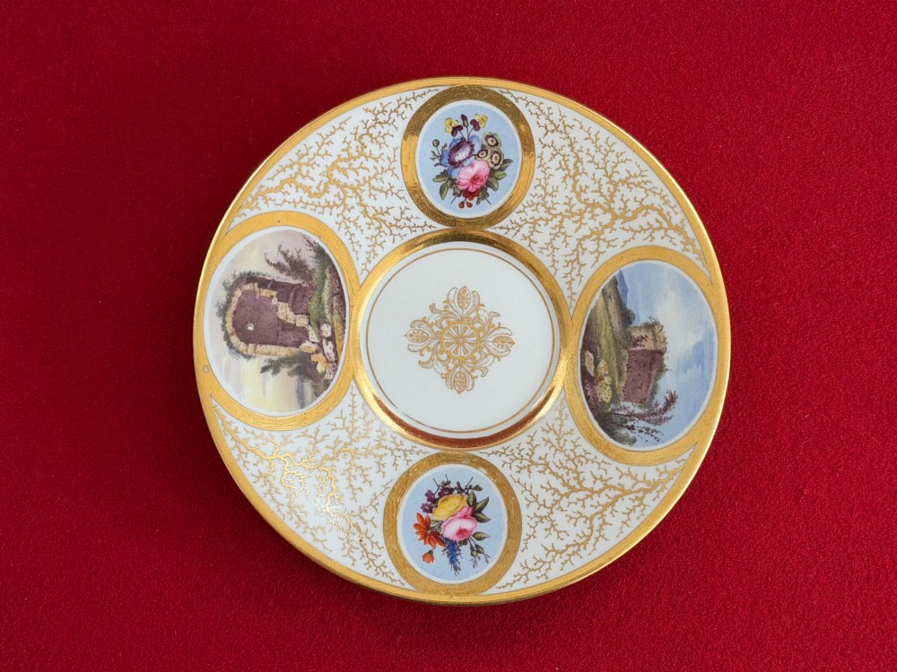An antique Flight, Barr and Barr Worcester porcelain covered chocolate cup with two handles and matching saucer, decorated with hand-painted landscape and floral panels amid gold vermicelli detailing. View V