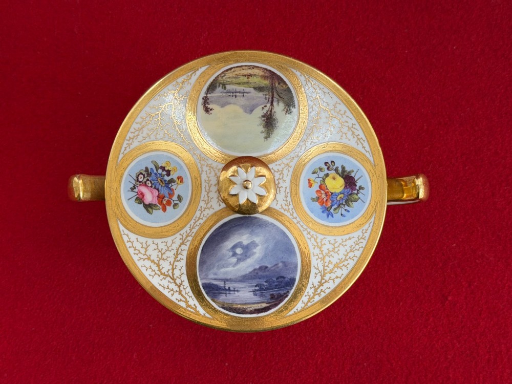 An antique Flight, Barr and Barr Worcester porcelain covered chocolate cup with two handles and matching saucer, decorated with hand-painted landscape and floral panels amid gold vermicelli detailing. View VII