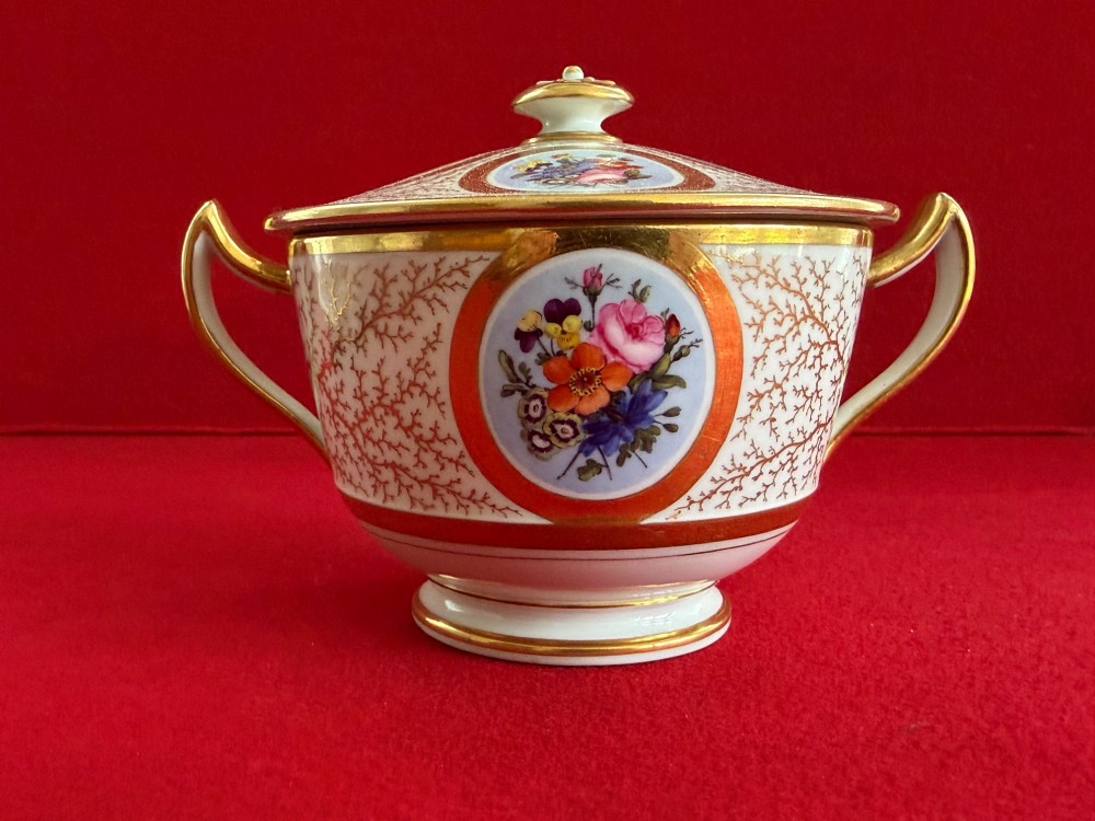 An antique Flight, Barr and Barr Worcester porcelain covered chocolate cup with two handles and matching saucer, decorated with hand-painted landscape and floral panels amid gold vermicelli detailing. View IX