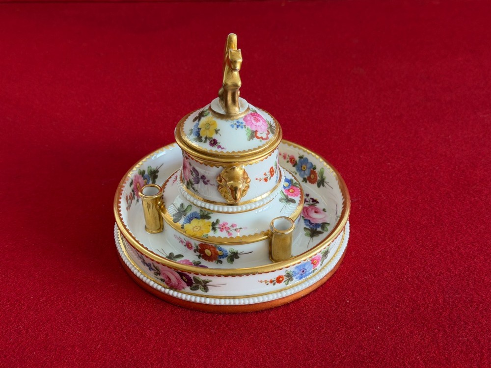 A circular white porcelain inkstand featuring hand-painted floral decoration, gilt accents, pen holders, and a cover topped with a golden griffin finial. View II