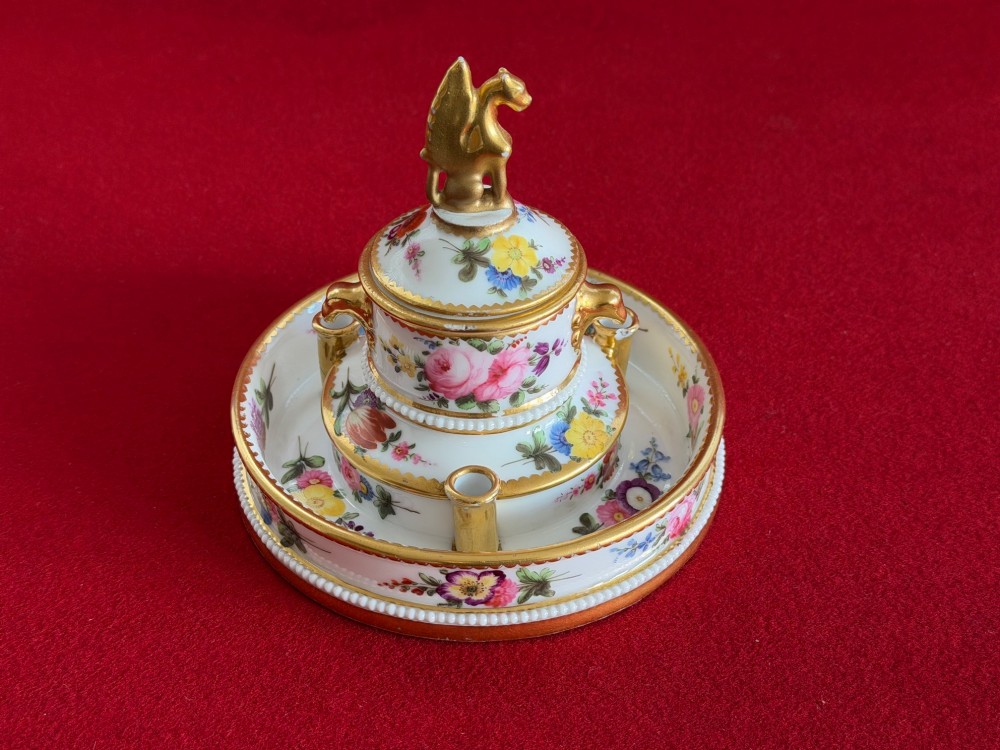 A circular white porcelain inkstand featuring hand-painted floral decoration, gilt accents, pen holders, and a cover topped with a golden griffin finial. View III