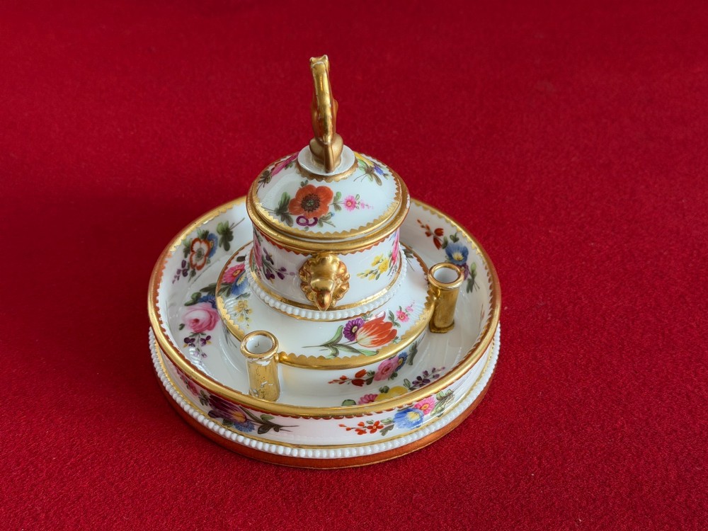 A circular white porcelain inkstand featuring hand-painted floral decoration, gilt accents, pen holders, and a cover topped with a golden griffin finial. View IV