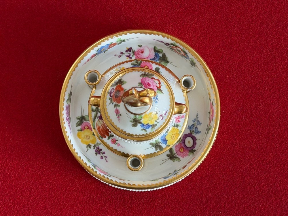 A circular white porcelain inkstand featuring hand-painted floral decoration, gilt accents, pen holders, and a cover topped with a golden griffin finial. View V