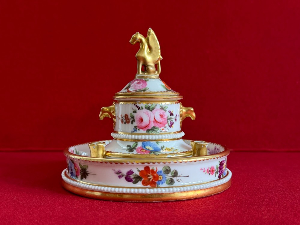 A circular white porcelain inkstand featuring hand-painted floral decoration, gilt accents, pen holders, and a cover topped with a golden griffin finial. View VII