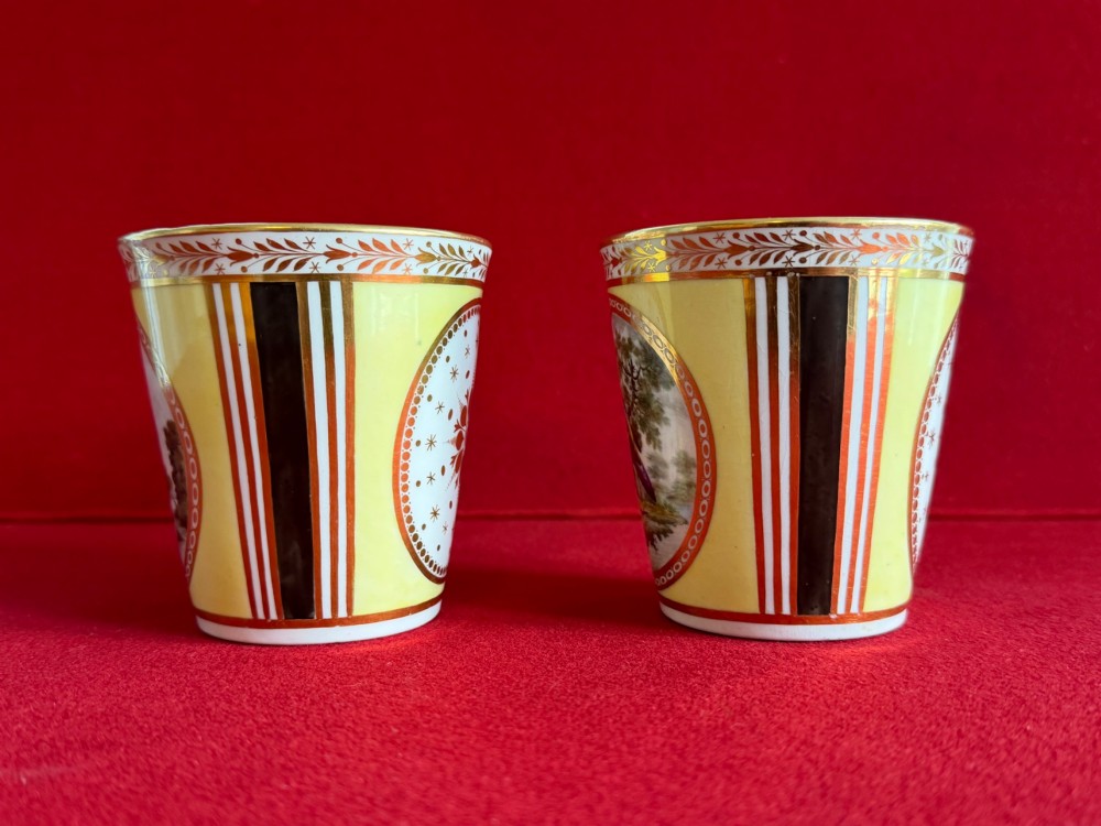 A pair of yellow antique porcelain beakers featuring hand-painted exotic birds within oval gilt reserves and gilded leaf borders along the top rim. View II