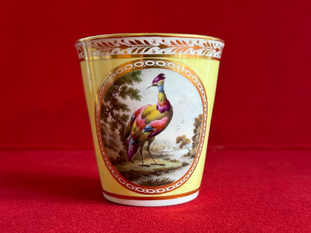 A pair of yellow antique porcelain beakers featuring hand-painted exotic birds within oval gilt reserves and gilded leaf borders along the top rim. View VI