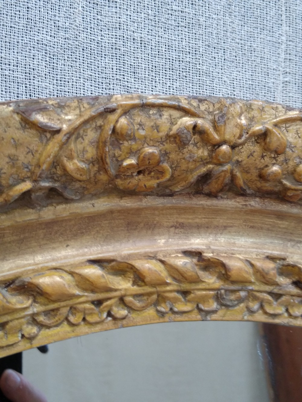 An antique oval wall mirror featuring a heavily hand-carved giltwood frame decorated with foliate and leaf moulding. View II