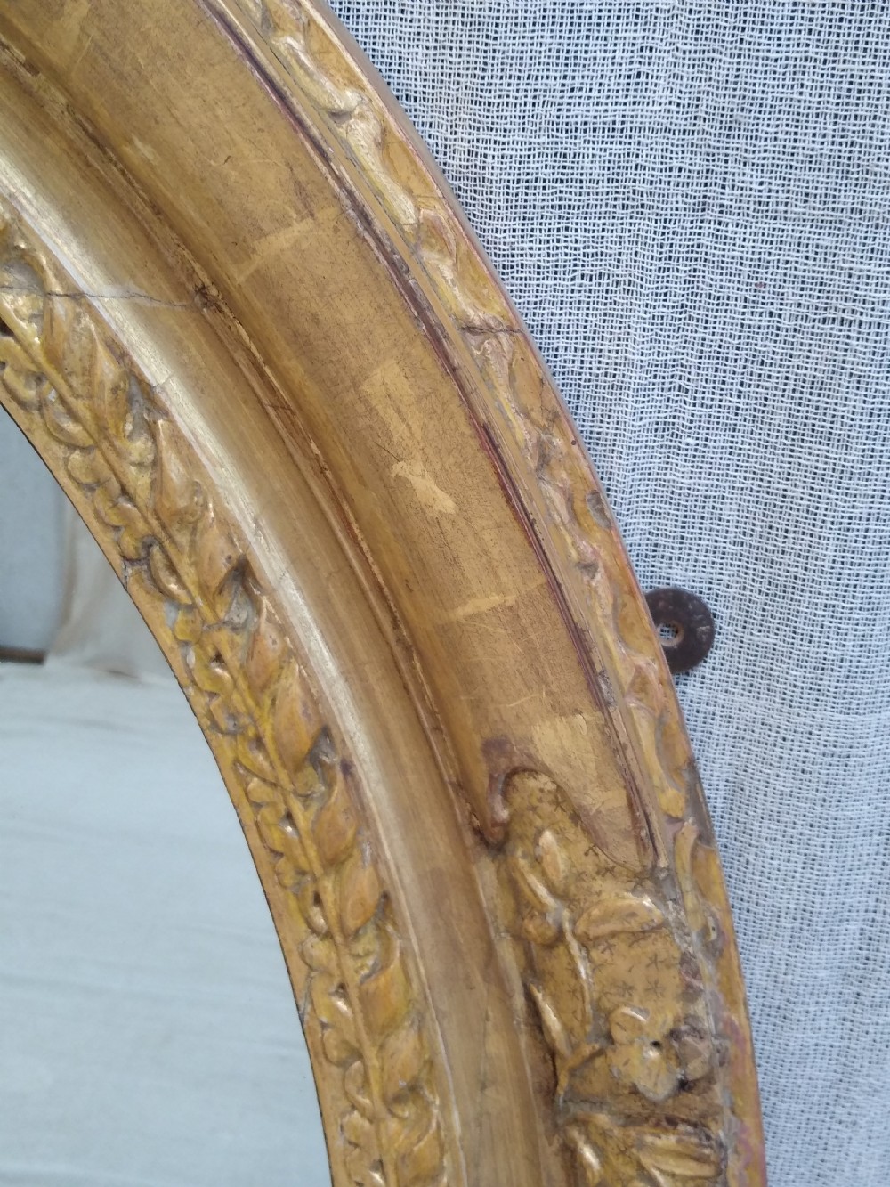 An antique oval wall mirror featuring a heavily hand-carved giltwood frame decorated with foliate and leaf moulding. View III