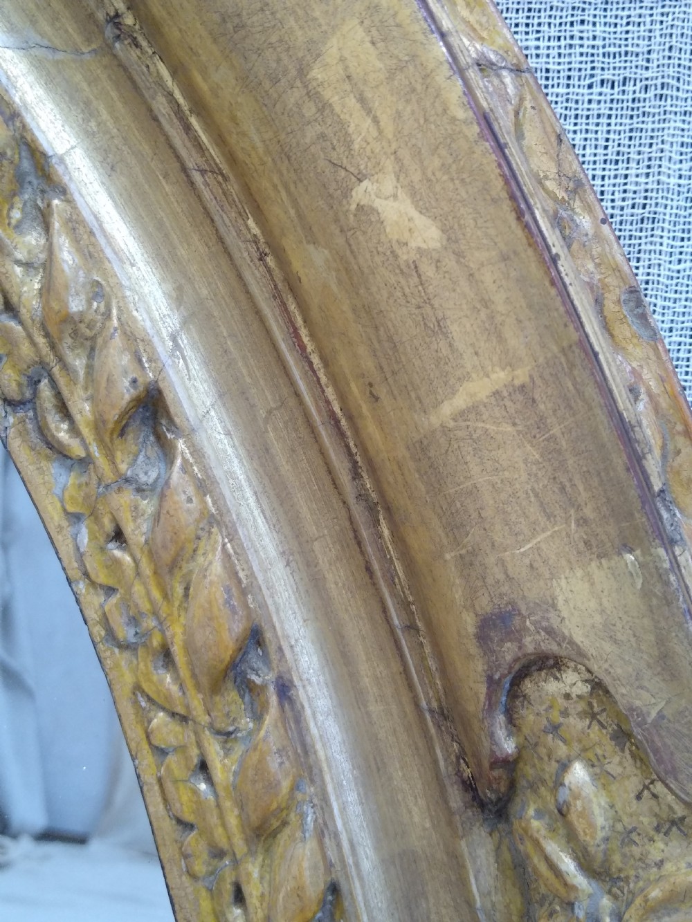 An antique oval wall mirror featuring a heavily hand-carved giltwood frame decorated with foliate and leaf moulding. View VI