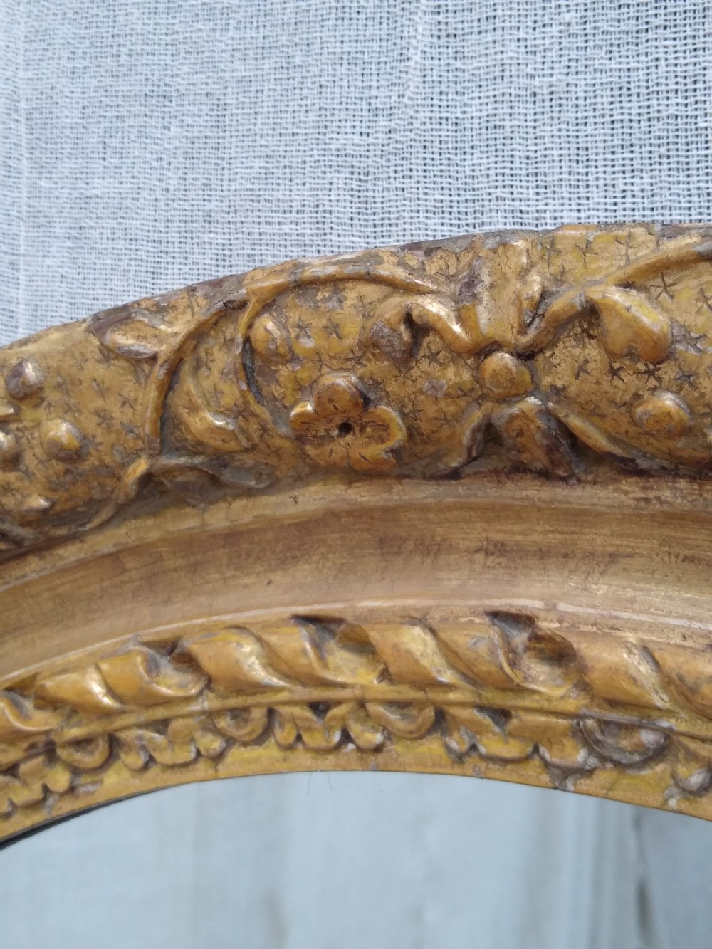 An antique oval wall mirror featuring a heavily hand-carved giltwood frame decorated with foliate and leaf moulding. View VII