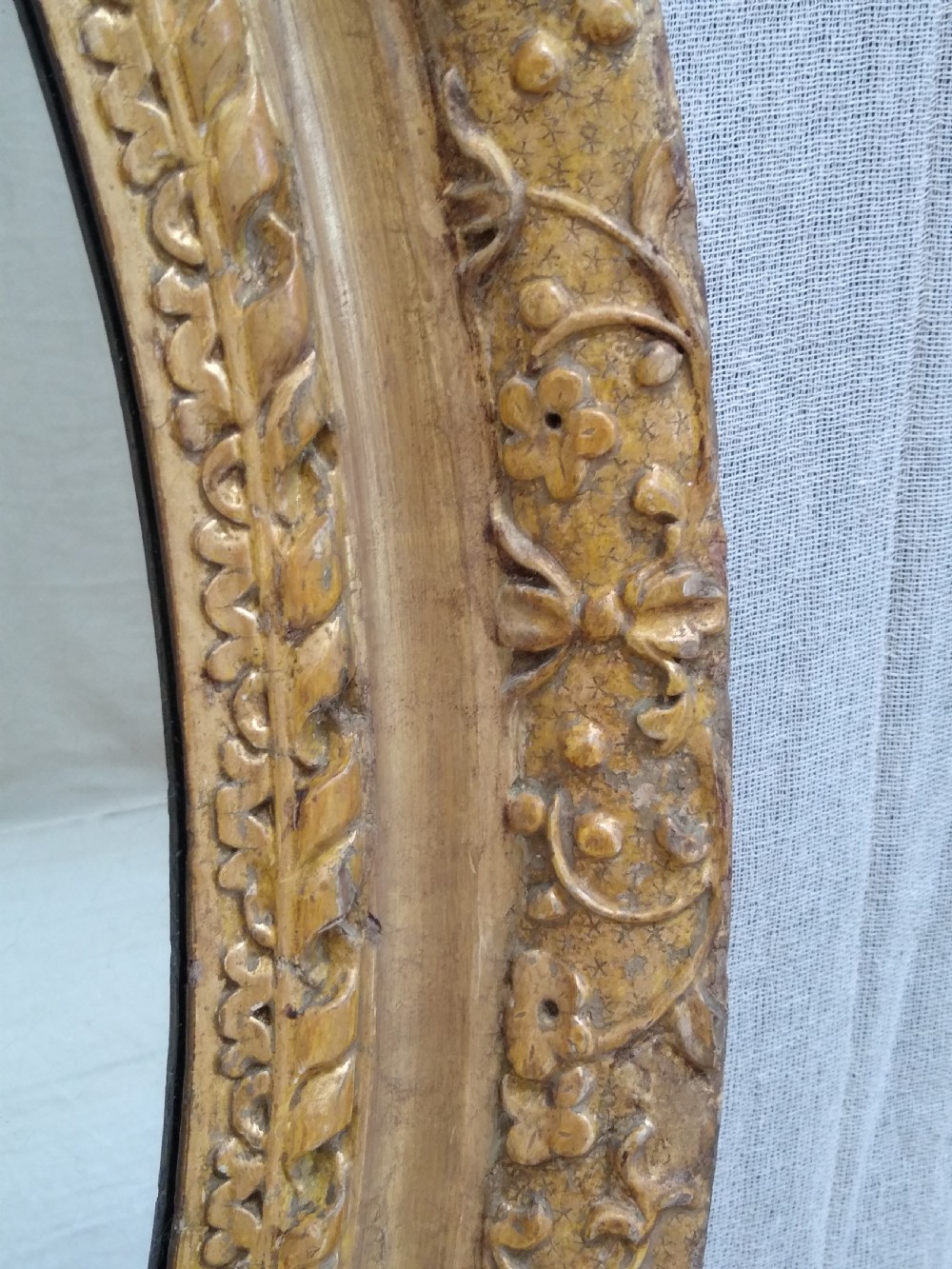 An antique oval wall mirror featuring a heavily hand-carved giltwood frame decorated with foliate and leaf moulding. View VIII