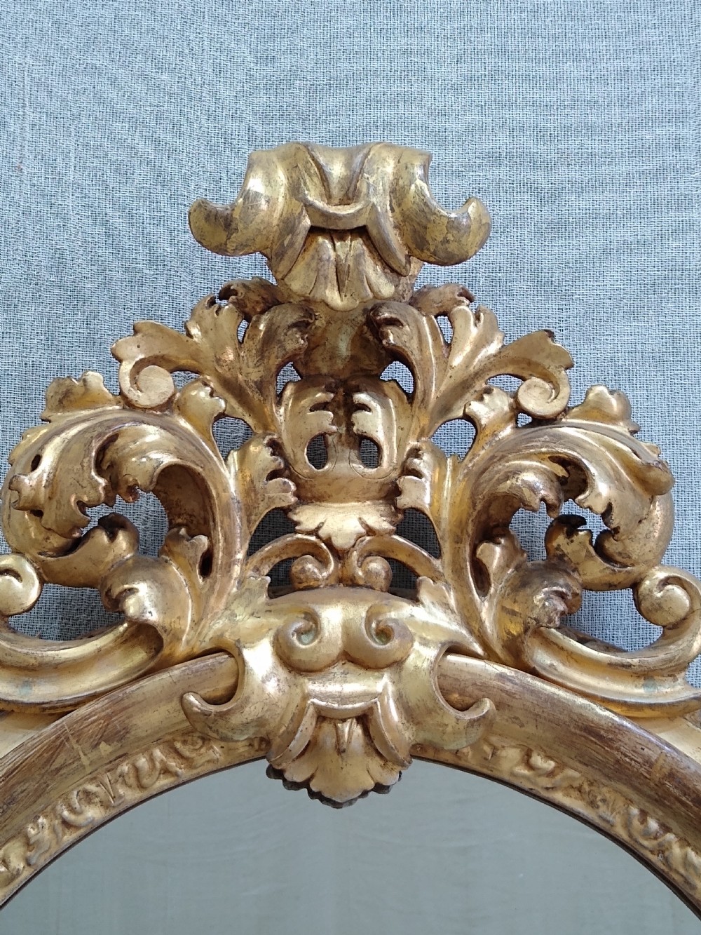 An antique 19th-century Italian oval giltwood wall mirror with an ornate carved scroll cresting pediment. View II