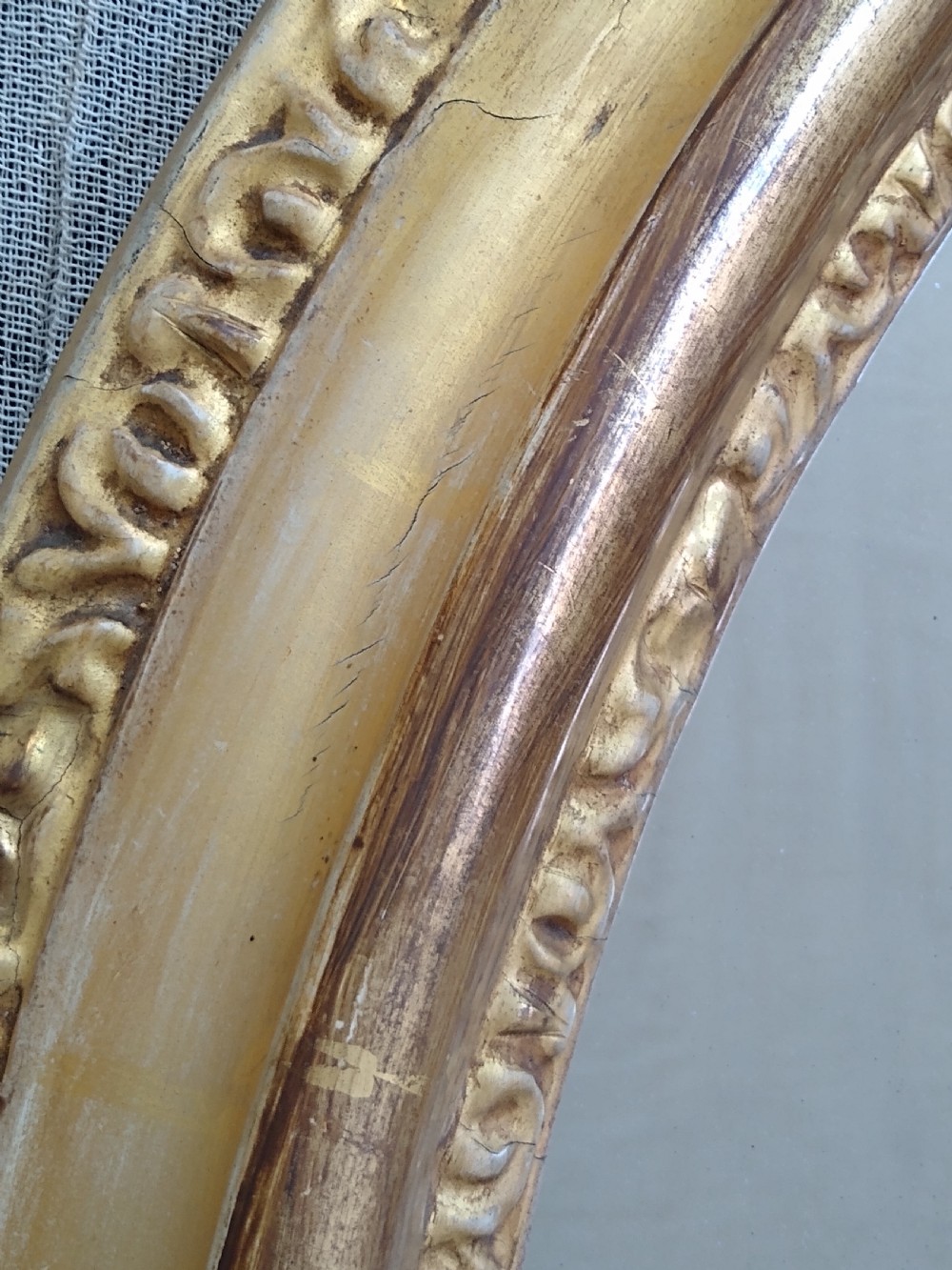 An antique 19th-century Italian oval giltwood wall mirror with an ornate carved scroll cresting pediment. View IV