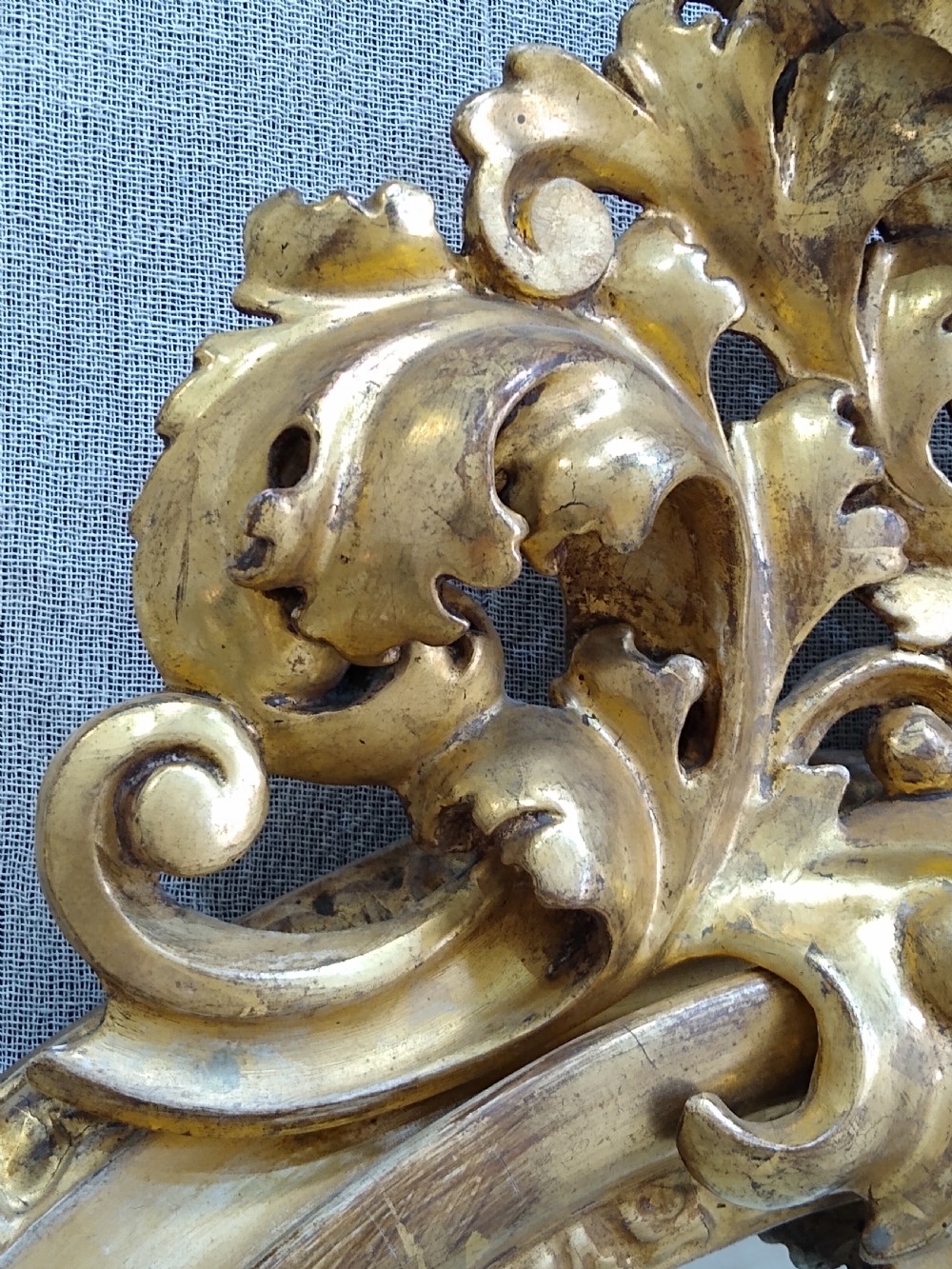 An antique 19th-century Italian oval giltwood wall mirror with an ornate carved scroll cresting pediment. View V