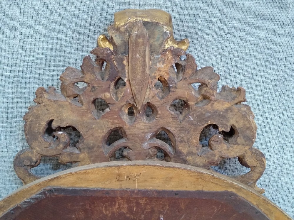 An antique 19th-century Italian oval giltwood wall mirror with an ornate carved scroll cresting pediment. View VI