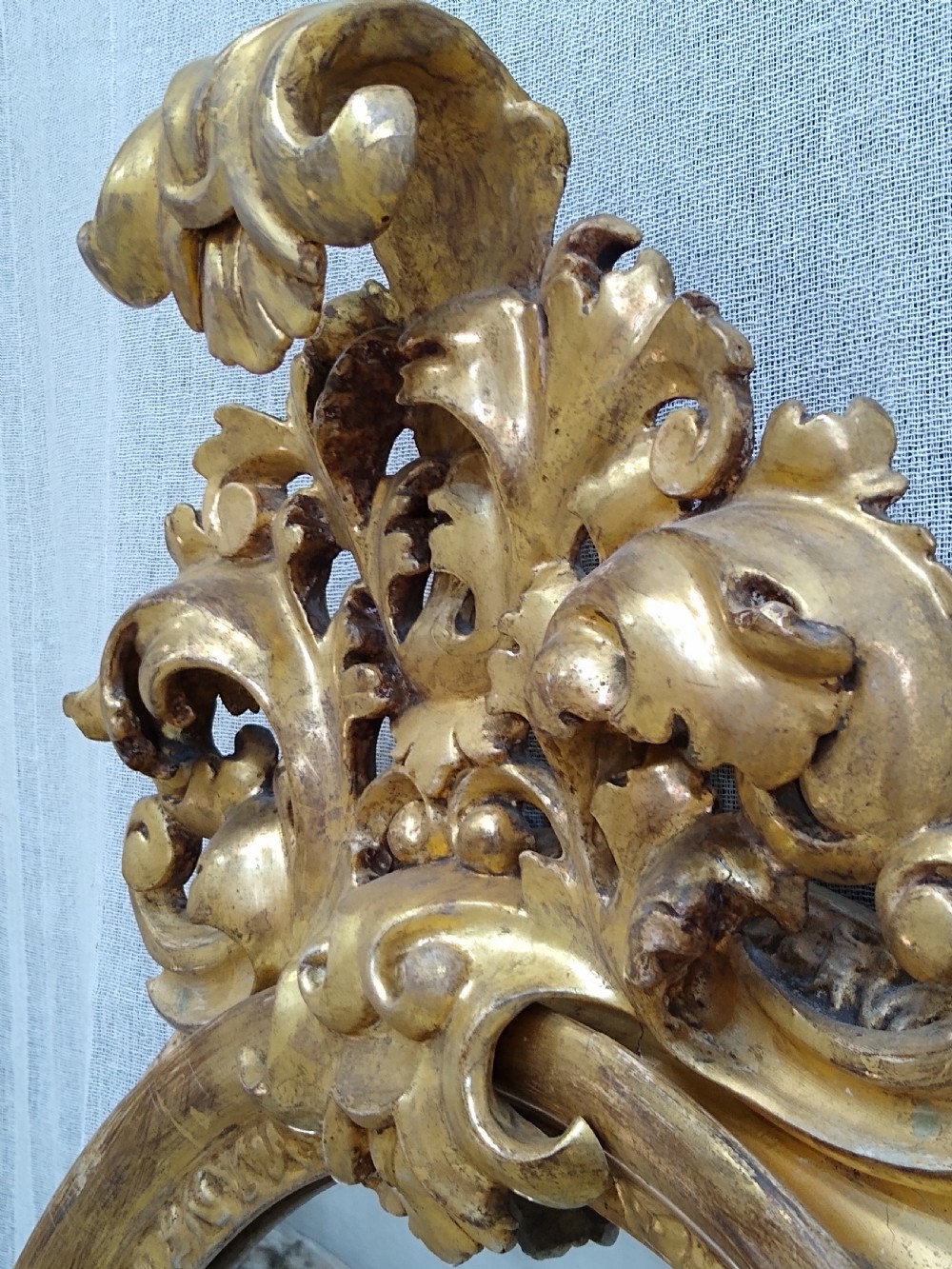An antique 19th-century Italian oval giltwood wall mirror with an ornate carved scroll cresting pediment. View VIII
