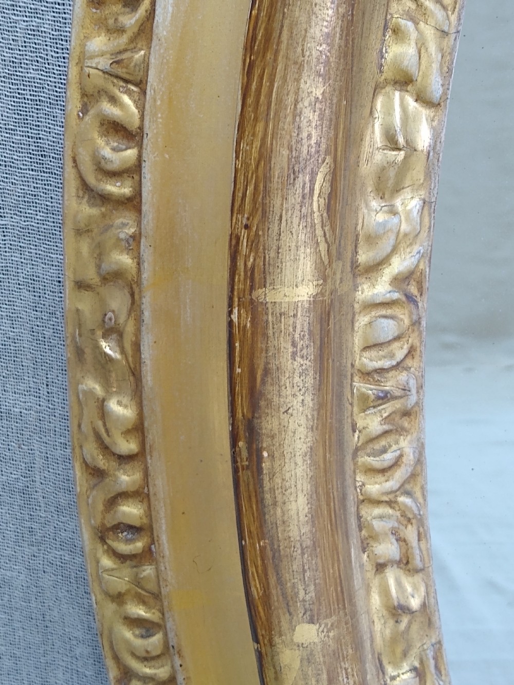 An antique 19th-century Italian oval giltwood wall mirror with an ornate carved scroll cresting pediment. View IX