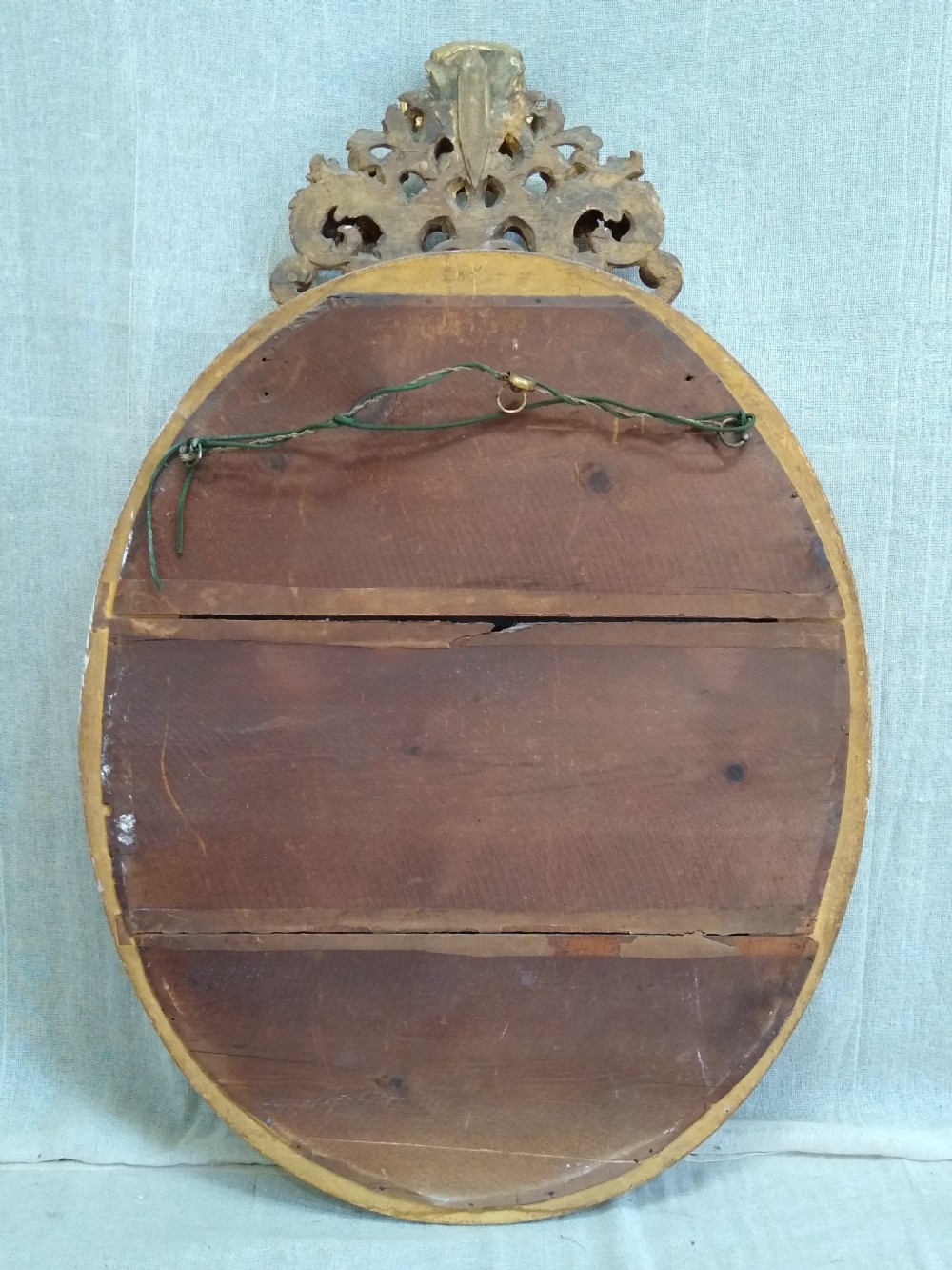 An antique 19th-century Italian oval giltwood wall mirror with an ornate carved scroll cresting pediment. View X