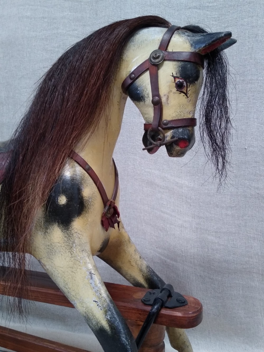 An antique carved wooden rocking horse with a painted dapple finish, leather saddle, and real horsehair mane, mounted on a wooden safety stand. View II
