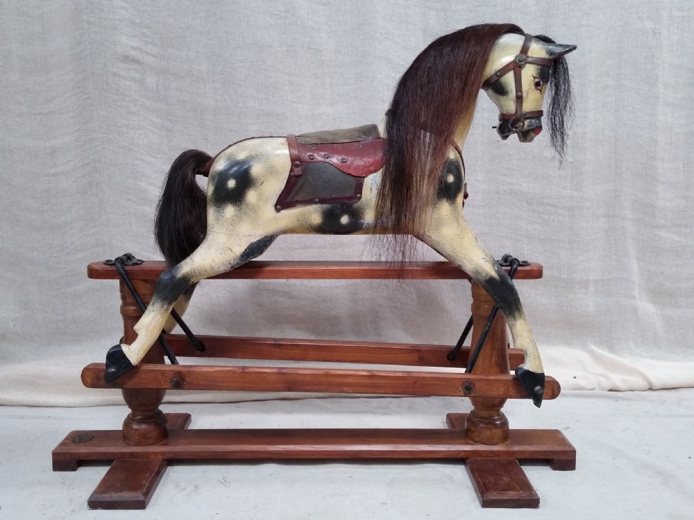 An antique carved wooden rocking horse with a painted dapple finish, leather saddle, and real horsehair mane, mounted on a wooden safety stand. View IV