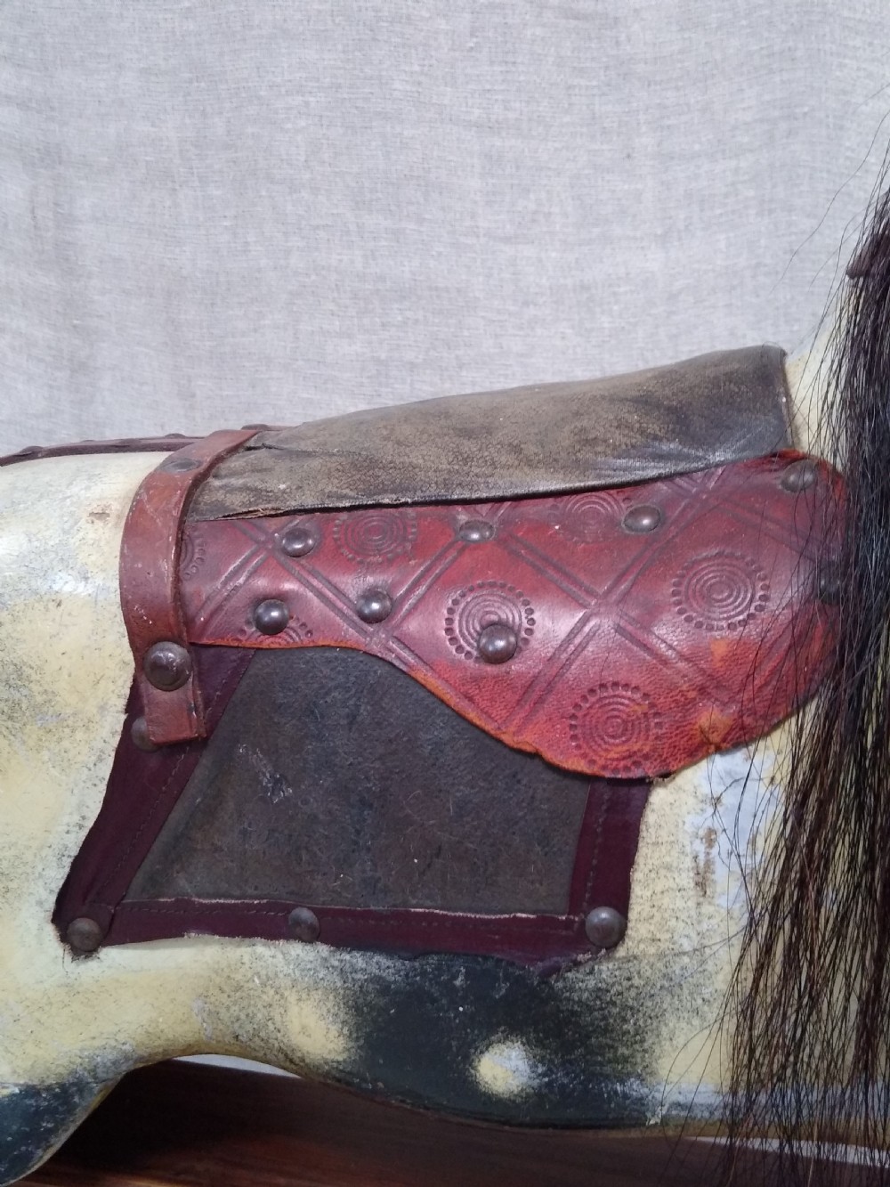 An antique carved wooden rocking horse with a painted dapple finish, leather saddle, and real horsehair mane, mounted on a wooden safety stand. View V
