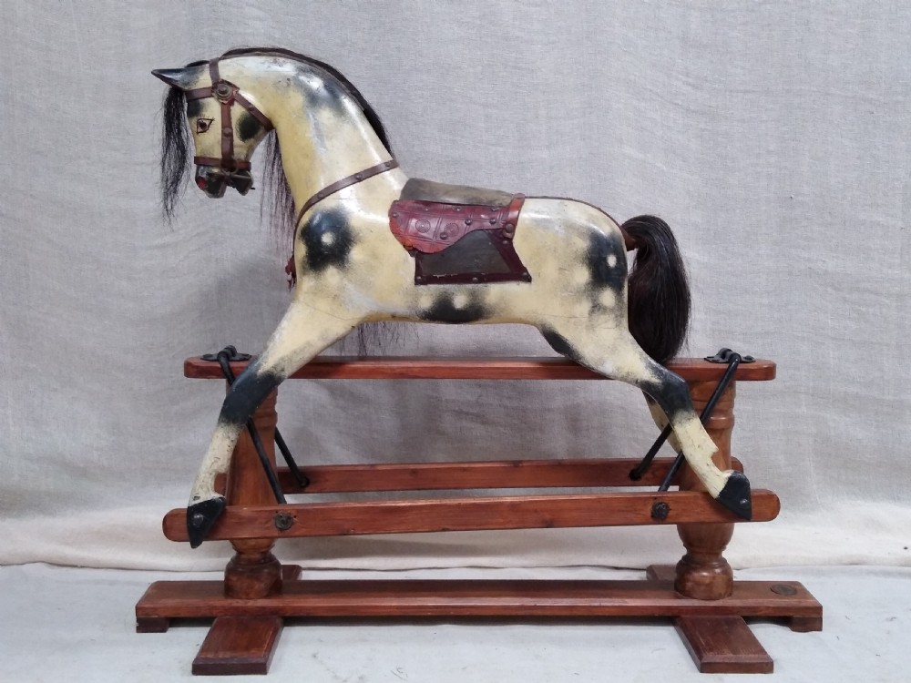 An antique carved wooden rocking horse with a painted dapple finish, leather saddle, and real horsehair mane, mounted on a wooden safety stand. View VI