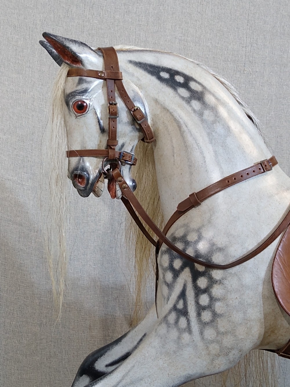 An antique carved wooden rocking horse with a dapple grey painted finish, real hair mane, leather saddle, and bridle, mounted on a wooden safety stand. View II