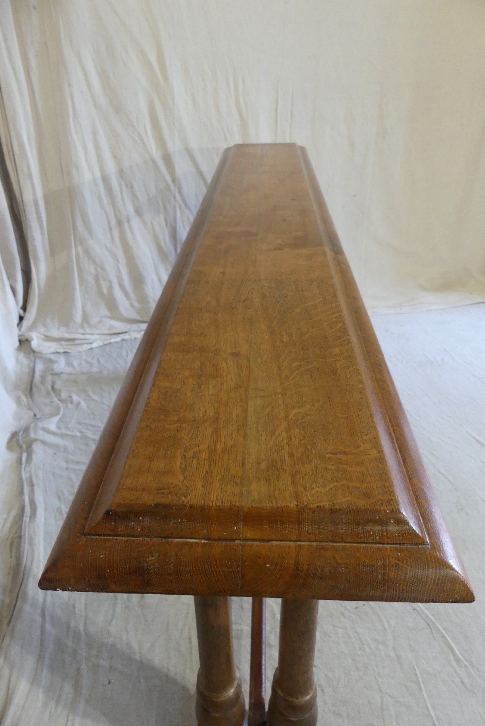 A long, narrow antique oak console table featuring a carved frieze, turned end supports, and a low central stretcher. View VI