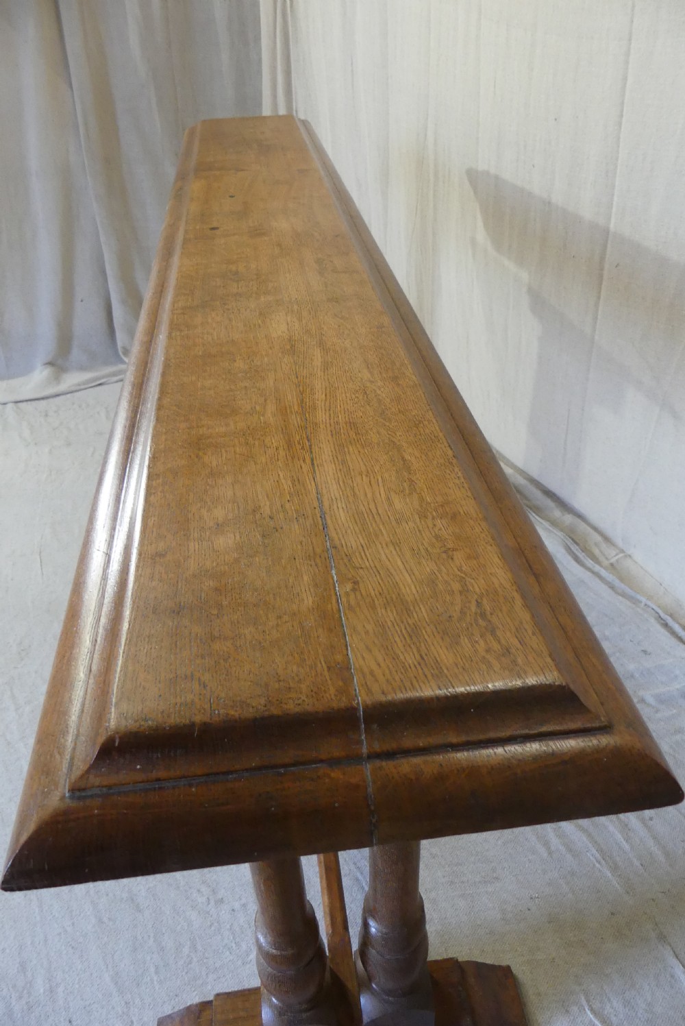 A long, narrow antique oak console table featuring a carved frieze, turned end supports, and a low central stretcher. View X