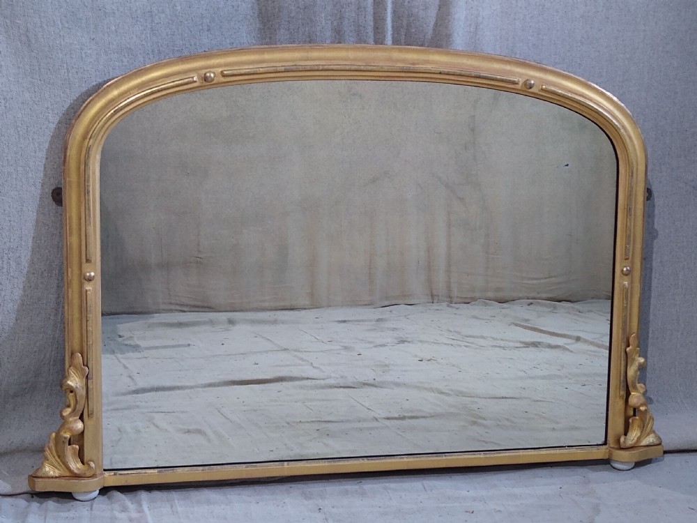 An antique Victorian arched overmantel mirror featuring a gilded frame with acanthus leaf corner details.
