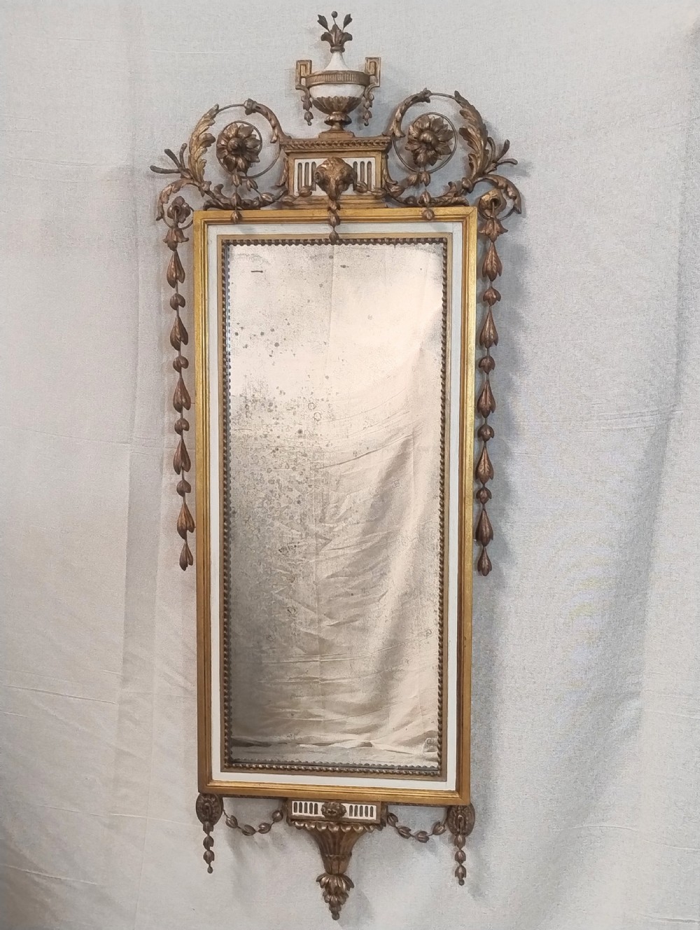 An Adam Revival parcel gilt pier wall mirror featuring an urn top cresting, decorative floral swags, side husk drops, and a rectangular gilded frame.