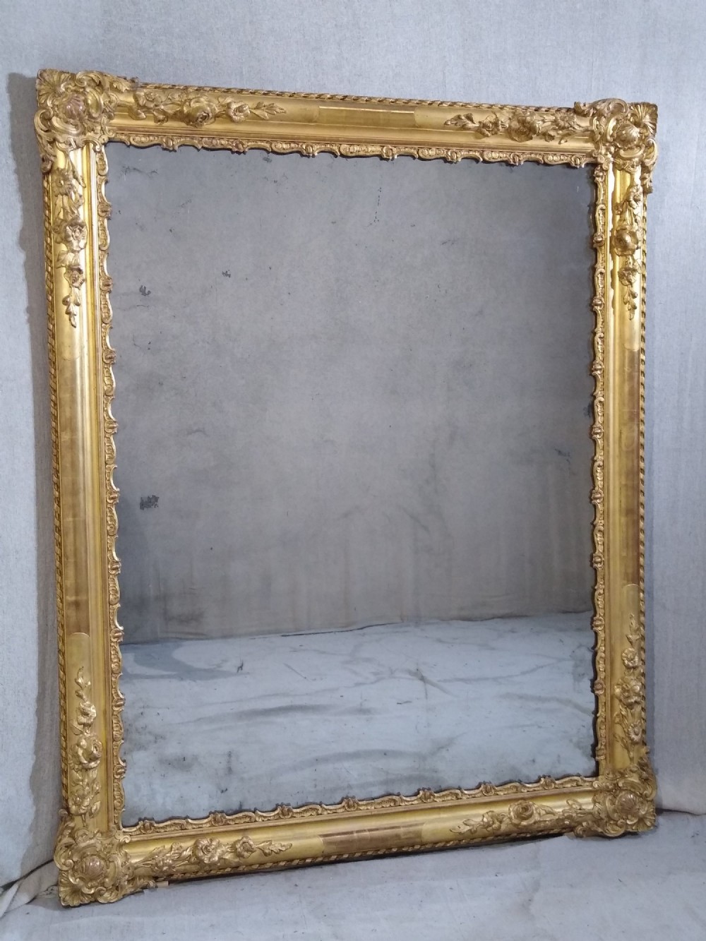 A large rectangular French antique wall mirror featuring a heavily decorated gold leaf frame with floral scroll mouldings.