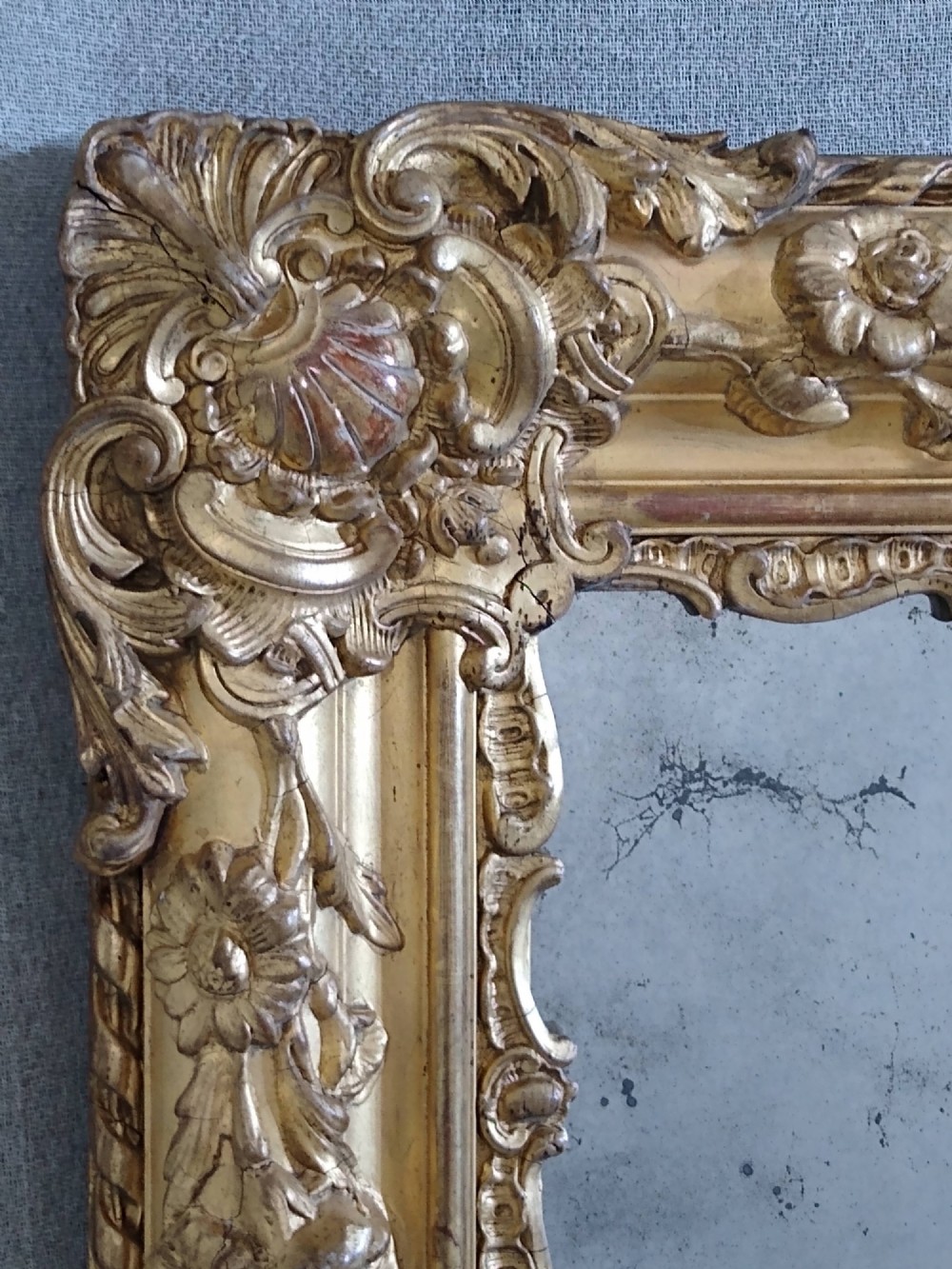 A large rectangular French antique wall mirror featuring a heavily decorated gold leaf frame with floral scroll mouldings. View V