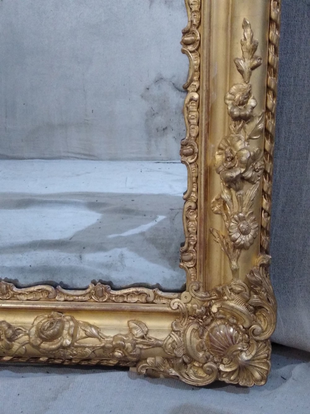 A large rectangular French antique wall mirror featuring a heavily decorated gold leaf frame with floral scroll mouldings. View VI