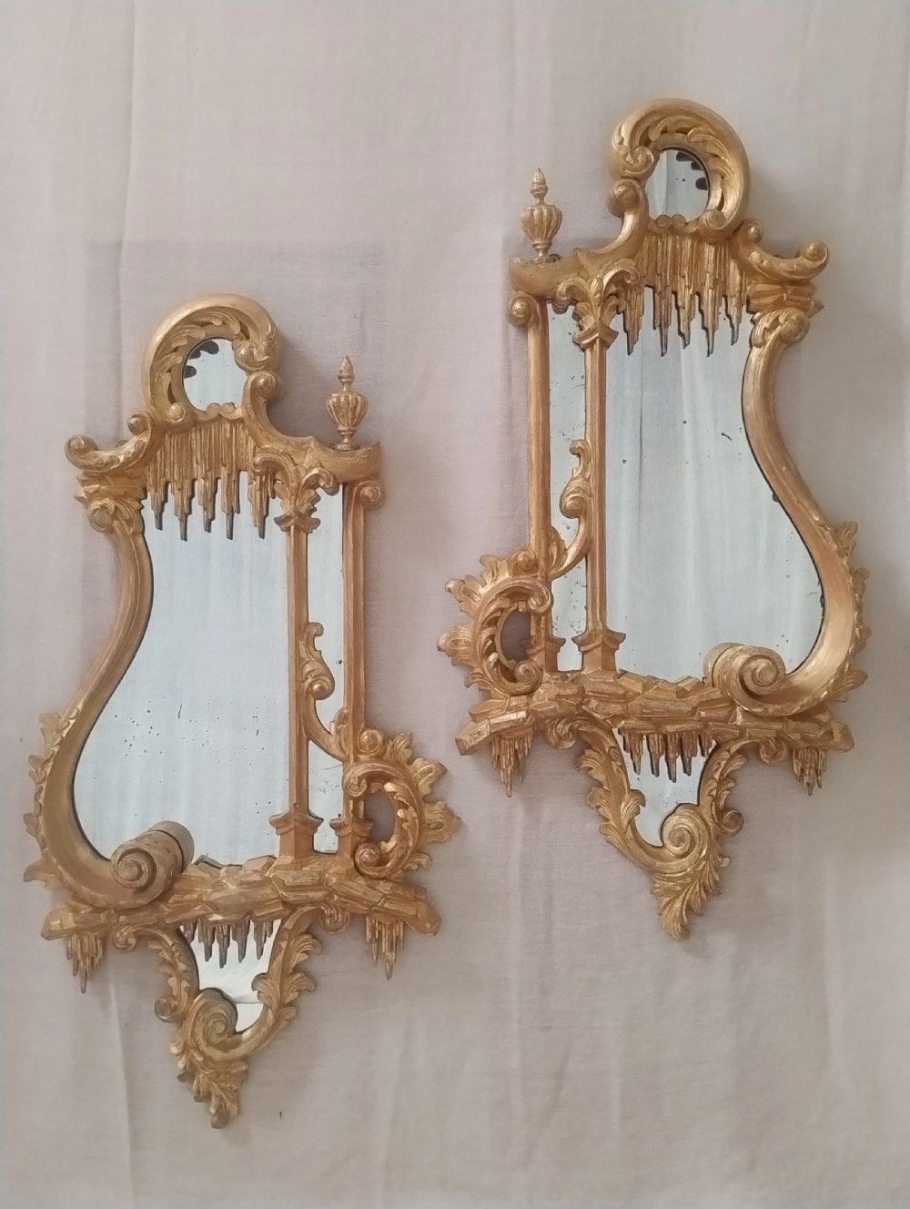 A pair of late 19th-century Chippendale Revival giltwood wall mirrors featuring ornate Rococo C-scrolls, foliage, and icicle carving.