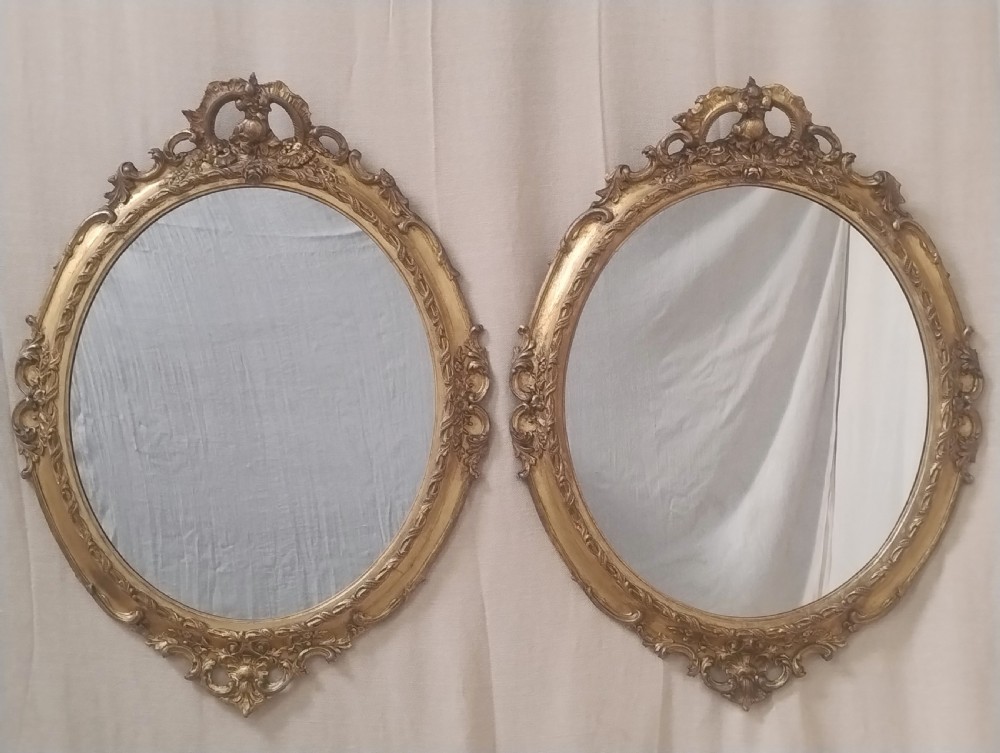 A pair of late Victorian oval wall mirrors featuring ornate carved giltwood frames with scrollwork cresting.