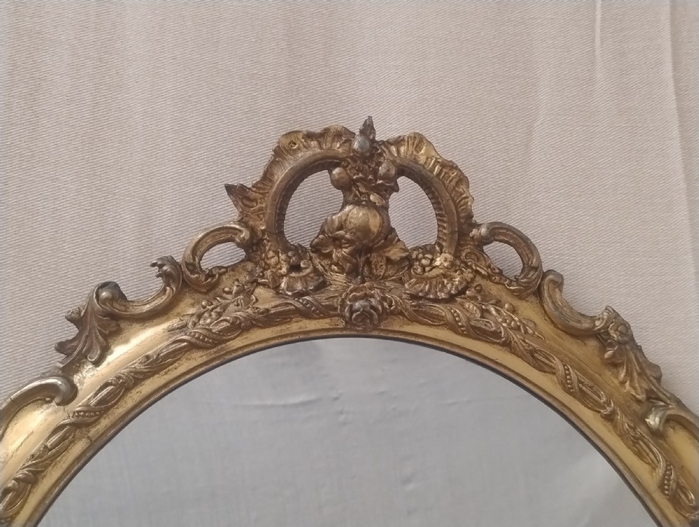 A pair of late Victorian oval wall mirrors featuring ornate carved giltwood frames with scrollwork cresting. View VI