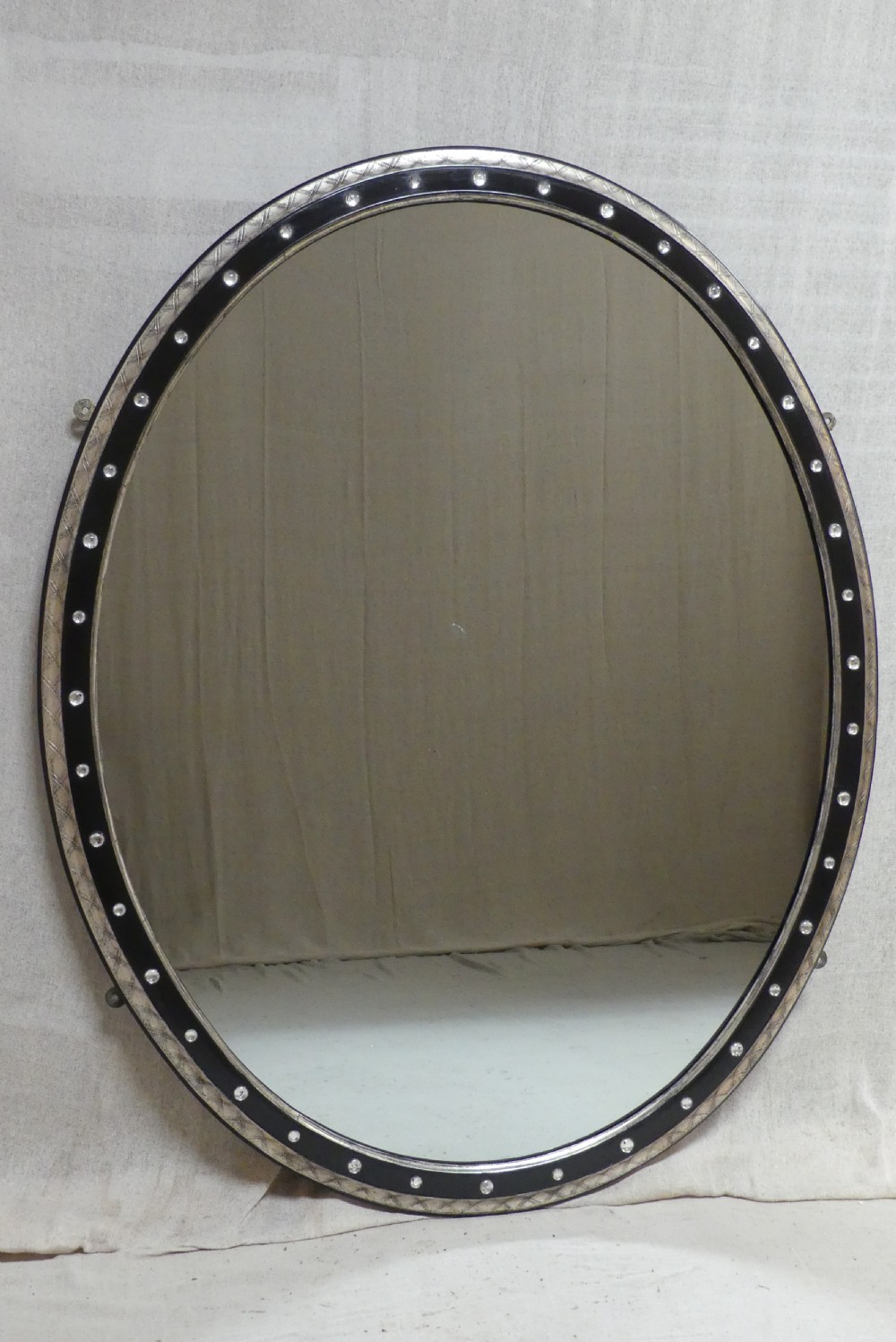 An antique oval wall mirror featuring a black ebonised band inset with round glass studs, framed by an engraved silvered border.