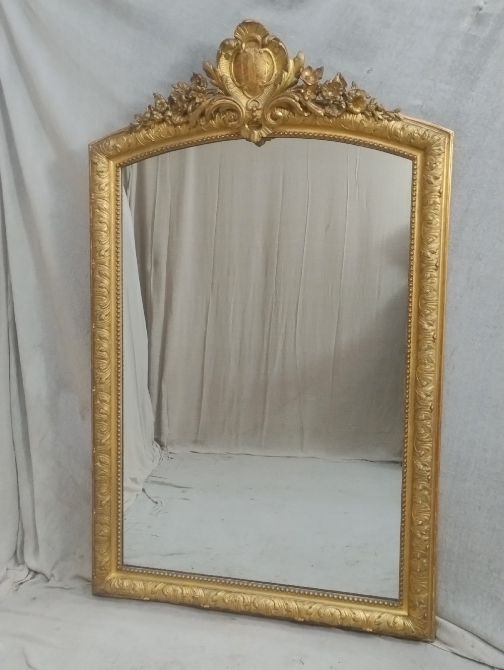 A large 19th-century French gilt mirror featuring an ornate floral cartouche cresting, gold leaf frame, and rectangular glass plate.