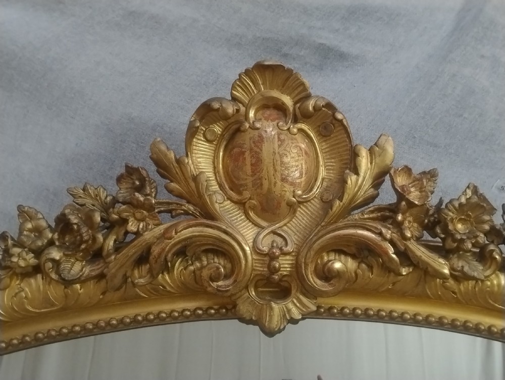 A large 19th-century French gilt mirror featuring an ornate floral cartouche cresting, gold leaf frame, and rectangular glass plate. View VI