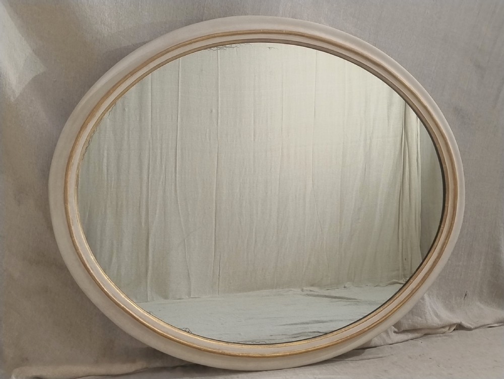 A large mid-19th-century oval wall mirror featuring a neutral off-white painted frame accented with a parcel gilt inner rim. View VI