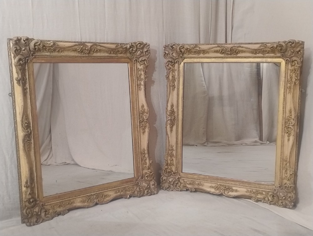 A matching pair of large late nineteenth-century wall mirrors featuring ornate carved rococo scrollwork frames with parcel gilt and cream paint finishes.