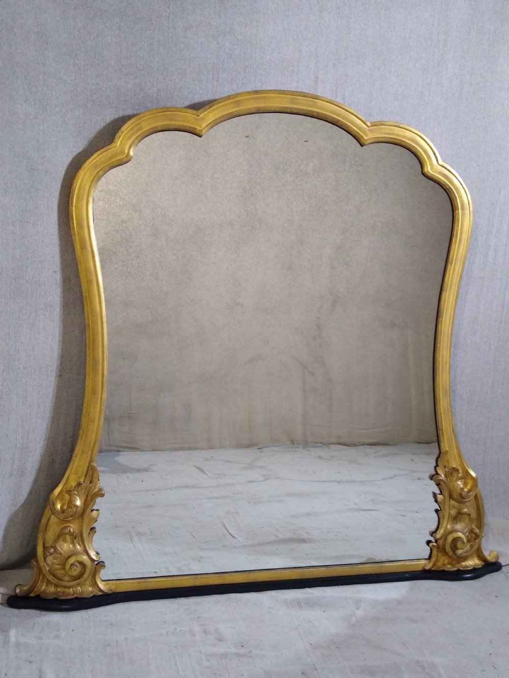 A large Victorian giltwood overmantel mirror featuring an arched top frame moulding and carved acanthus leaf scroll embellishments at the lower base corners.