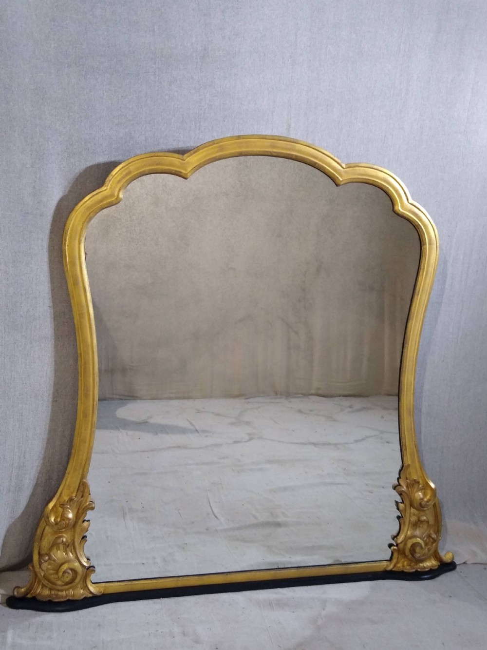 A large Victorian giltwood overmantel mirror featuring an arched top frame moulding and carved acanthus leaf scroll embellishments at the lower base corners. View II