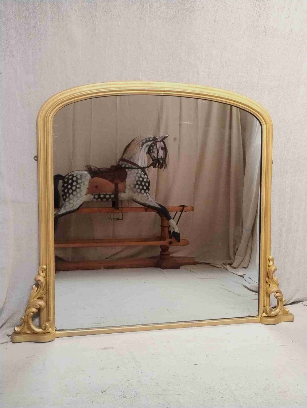 A large 19th-century Victorian giltwood overmantel wall mirror featuring an arched top and ornate acanthus leaf scroll feet.