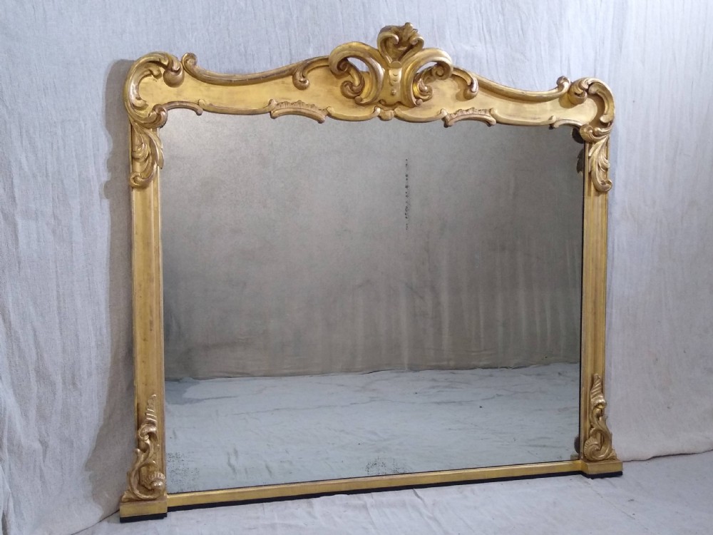 A large mid-nineteenth century giltwood overmantel mirror featuring elaborate scrolled cresting and decorative corner accents.